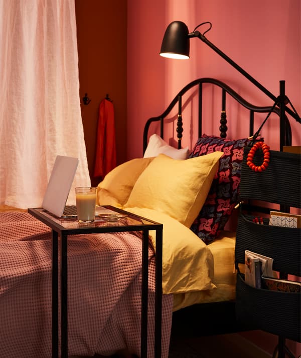 Wide bed divided down the middle by a curtain hanging just over it, with one side of the bed equipped as a workspace.
