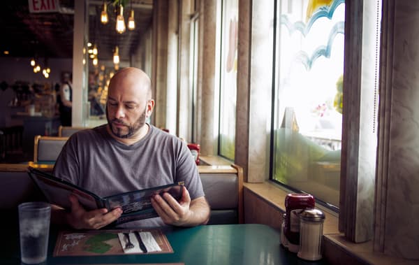 William sits in a diner looking at a menu.