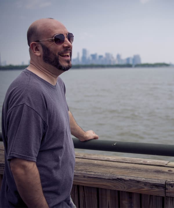 William stands looking across the water with a city skyline in the background.