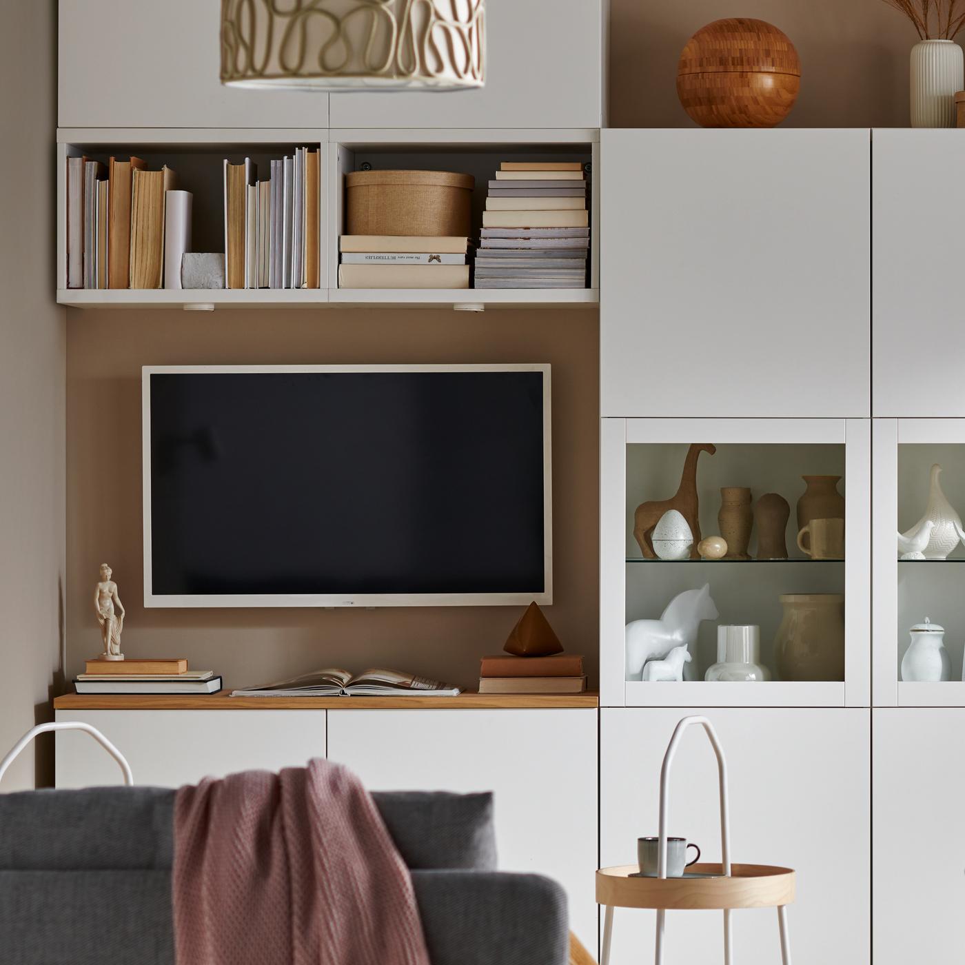 Wit BESTÅ tv-meubel staat onder een wandgemonteerde tv, met nog andere kasten uit het BESTÅ systeem erboven en aan één kant opzij.