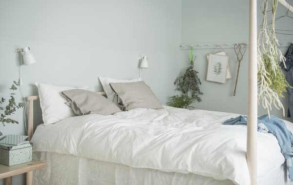 Wit en beige textiel in een GJÖRA berken bed met laag hoofdeinde en hoog voeteinde, met twee spots aan de wand