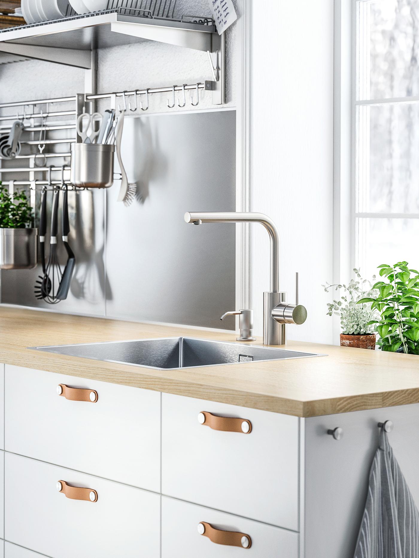 Witte kasten met witte ladefronten en ÖSTERNÄS lederen handgrepen onder een houten werkblad met gootsteen en een mengkraan.