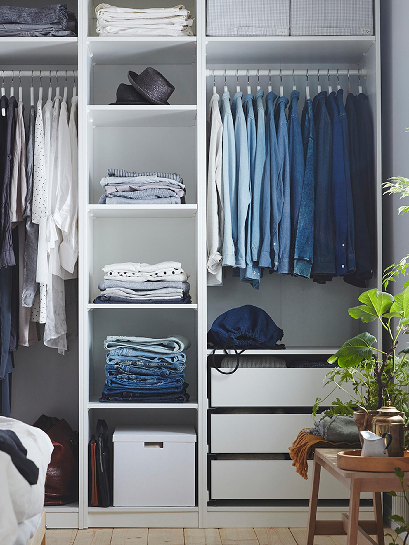 Witte PAX kleerkast met heel veel kleren, waaronder hoofddeksels en gevouwen kleding op de planken en shirts hangend aan de roedes.
