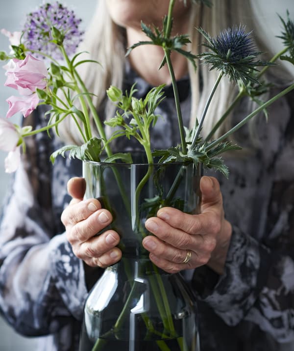 Woman holding a glass vase with some flowers in it.