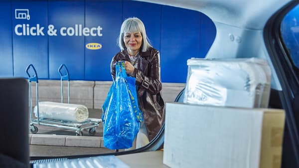 Woman loading IKEA products into her car at a Click & Collect station, holding a large blue IKEA shopping bag