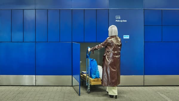 Woman placing IKEA items into a blue Pickup Box using a shopping trolley, as part of the self-service pickup system