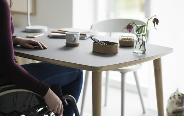 Woman sat in a wheelchair at an OMTÄNKSAM table.