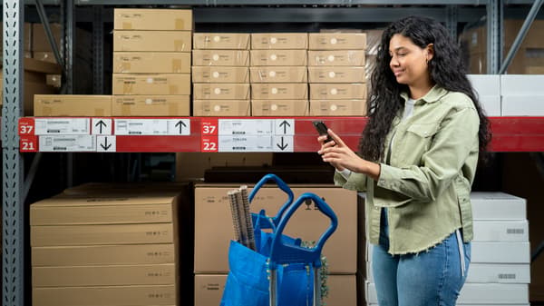 Woman smiling while looking at her phone between the shelves of the IKEA Self-Service Warehouse.