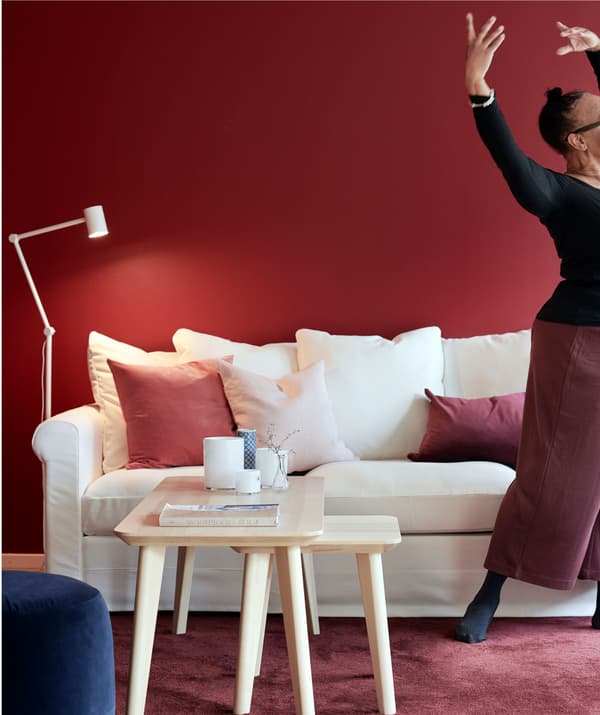 Woman striking a graceful dance pose, standing next to a sofa. White-and-red matching furniture, wall, rug and details.