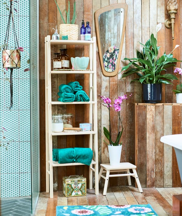 Wood spa-style bathroom with green-tiled walk-in shower, a wood shelf unit with green rolled towels and jars and plants.