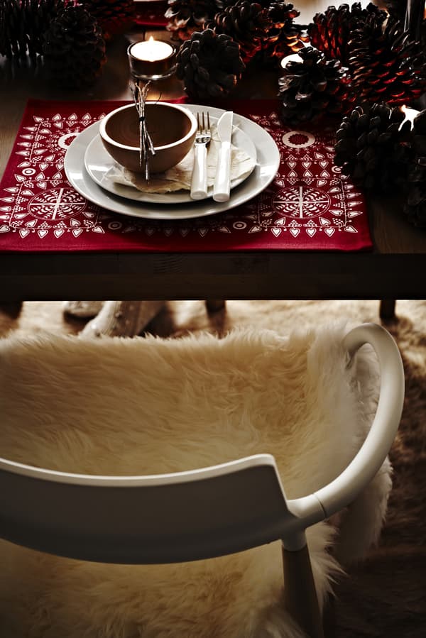  Wooden chair covered in a fluffy rug beside a festive table setting with candles. 