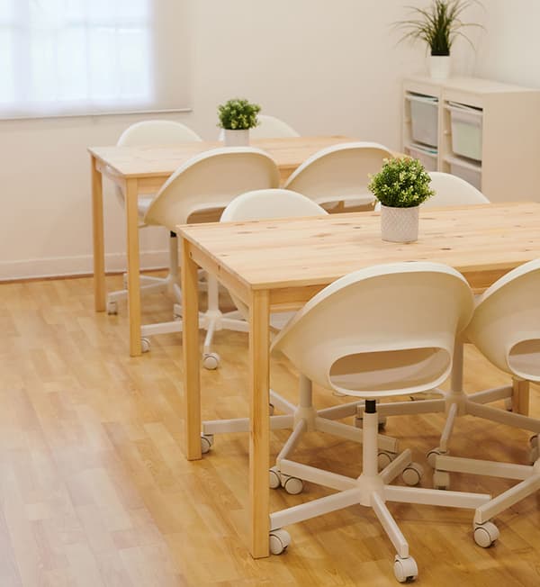 Wooden tables with a decorative potted plant placed on top with white chairs tucked into the table.