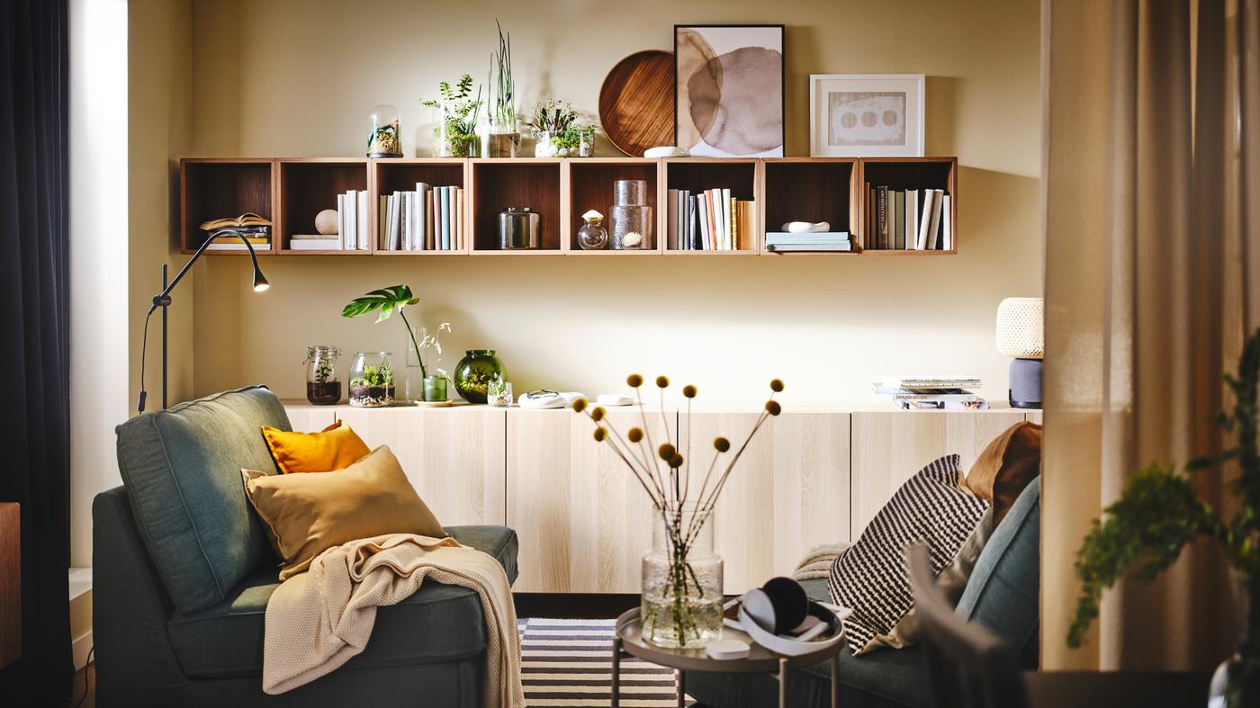 Woonkamer met KIVIK fauteuils die tegenover elkaar staan. Aan de tegenovergestelde wand hangt een rij EKET open kasten met boeken.