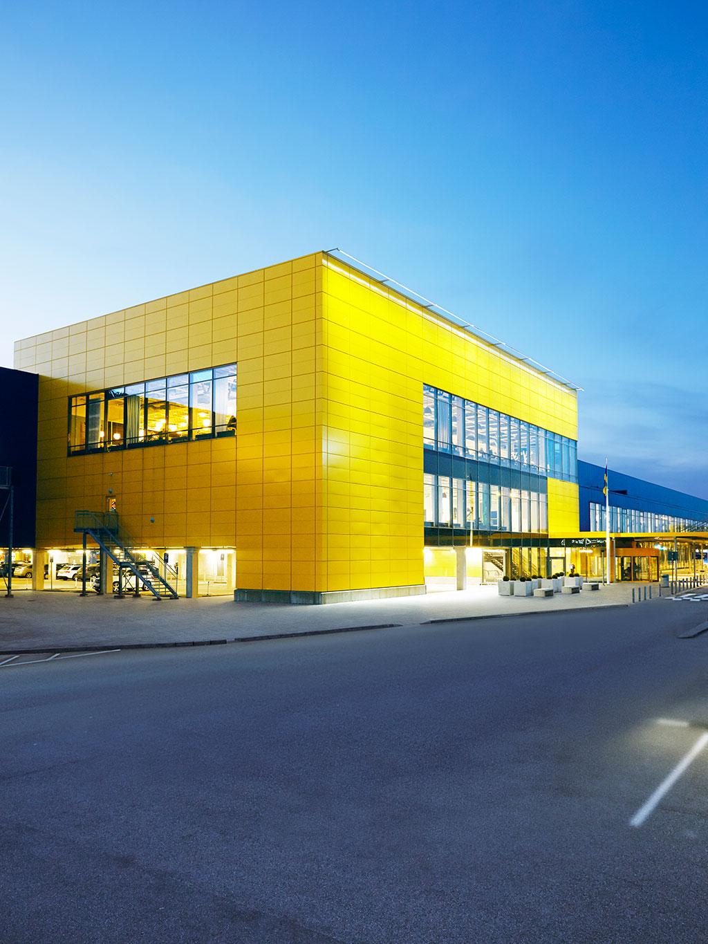 Yellow and blue furniture store building at dusk, brightly lit with large windows and clean, modern lines.