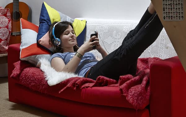 young girl reclined on a red sofa listening to music