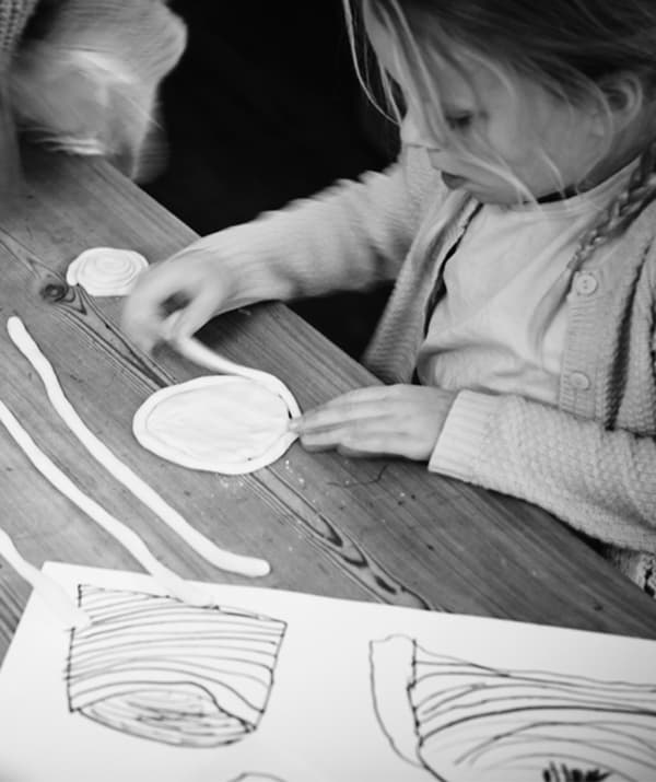 Young girl standing by a table, engrossed in twirling long strings of dough into disc-shaped creations ready for the oven.
