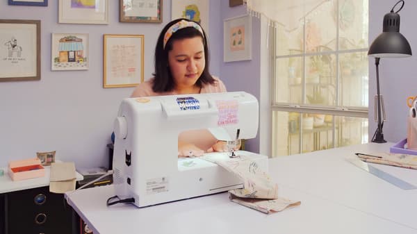 Young woman sits in a tidy organised room, using a sewing machine to create something.