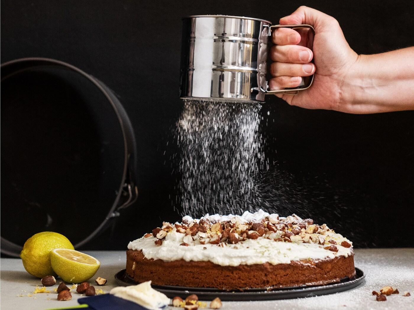 يستخدم بيكر مقشطة مطاطية BAKGLAD زرقاء من ايكيا لتزيين كعكة على حامل كعك زجاجي ARV BRÖLLOP.