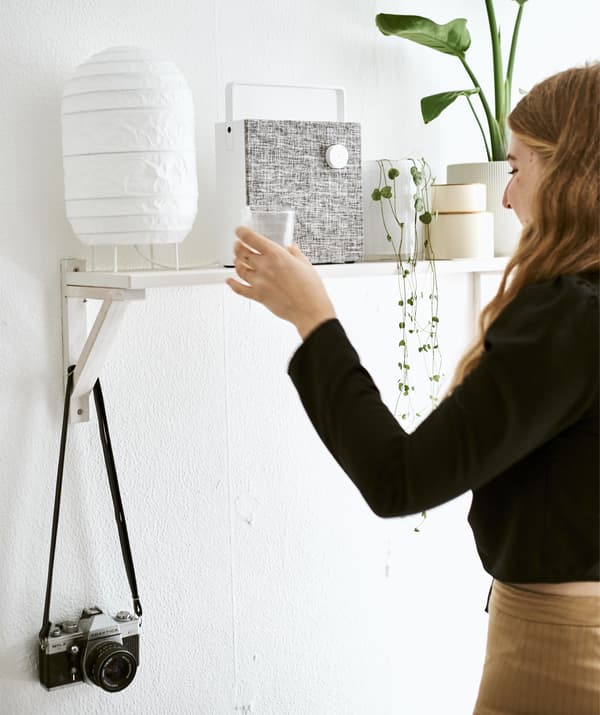 Yvet dépose son verre sur une étagère où sont placés une lampe, des plantes et un haut-parleur.
