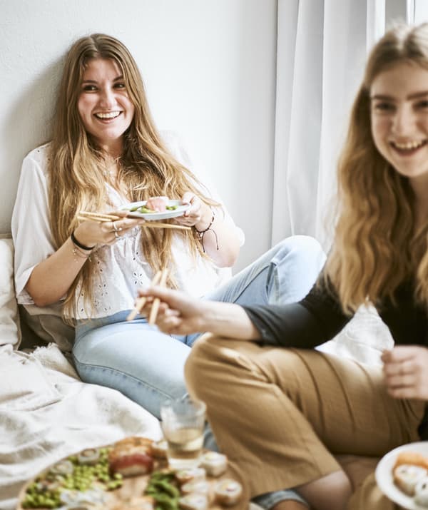Yvet et son amie assises sur le lit autour d’un plat de sushis.