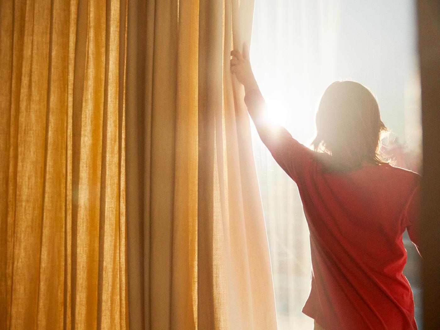 Žena povlači zavesu da pozdravi sunce.