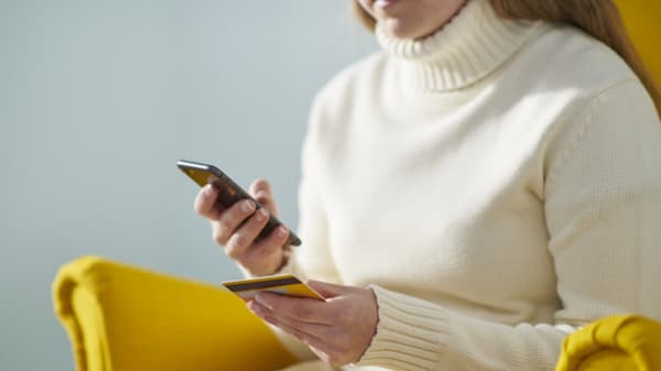 Žena ve žlutém křesle IKEA si na mobilním telefonu kontroluje své finance