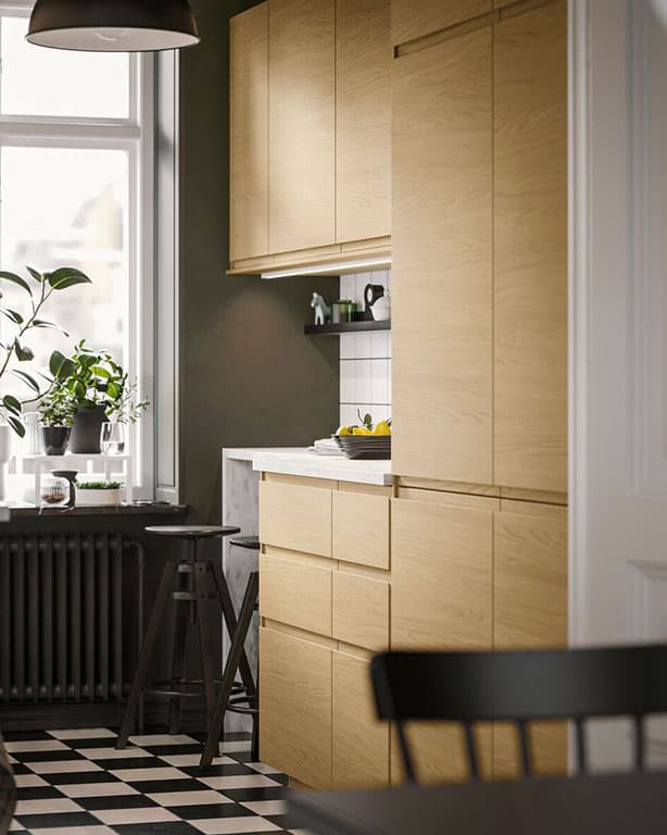 zu sehen ist eine IKEA Küchenlösung mit Fronten aus Holz, im vordergrund ein schwarzer Esstisch sowie Stuhl und im hinteren teil des Bildes ein Fenster mit einer Topfpflanze.