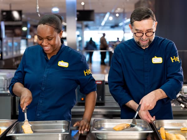 Zwei IKEA Mitarbeitende unterhalten sich während eine Person im Gabelstapler sitzt und die andere einen Leitkegel hält.