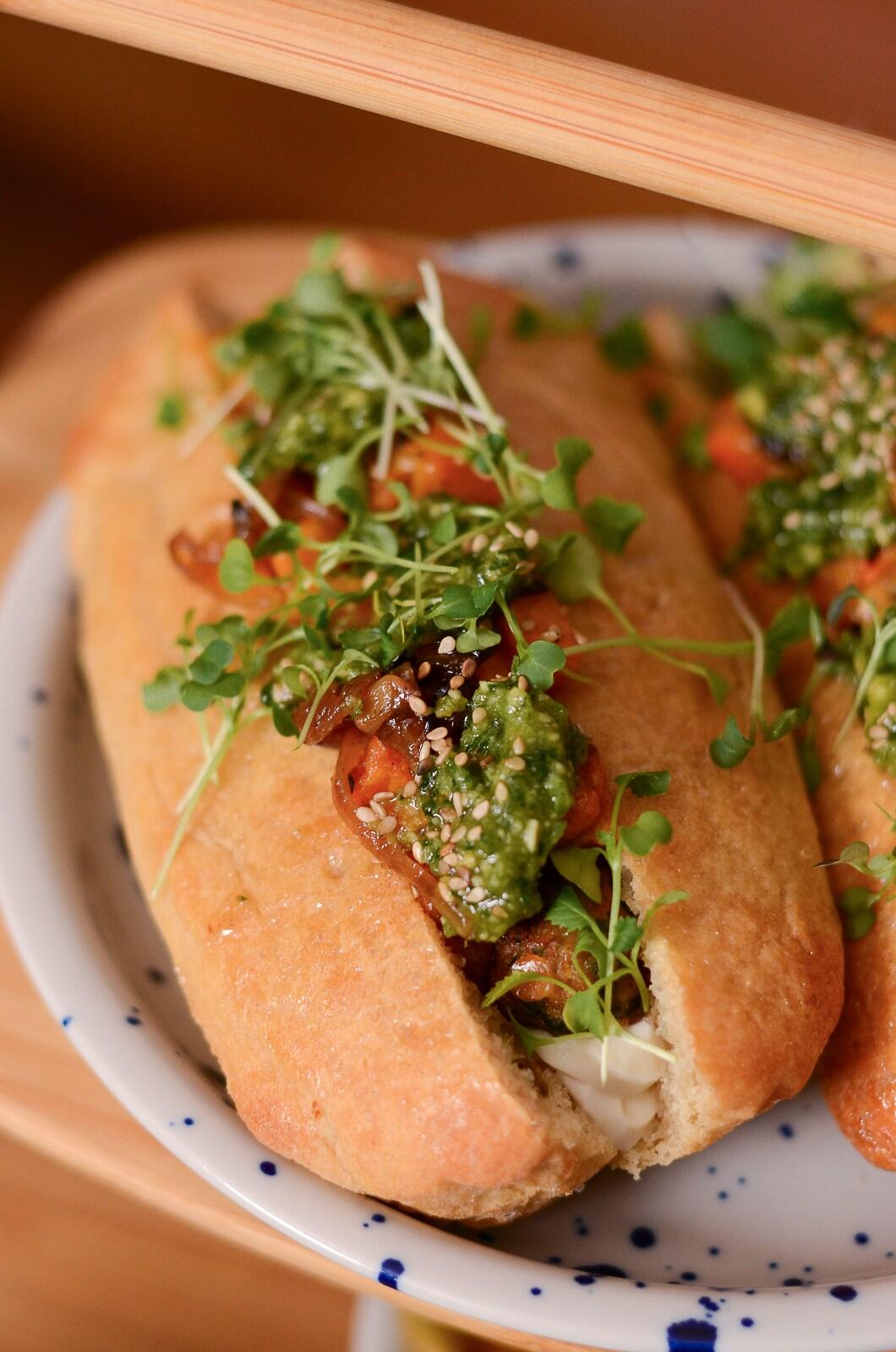 Zwei leckere Sandwiches mit Kräutern, Pesto und Microgreens auf einem bunten Teller, dazu gibt's Essstäbchen.