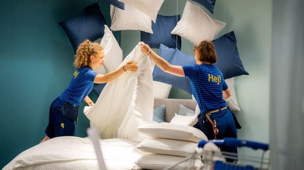 Zwei Leute in blauen IKEA Hemden richten grosse, flauschige Kissen und Bettzeug in einem coolen Showroom her.