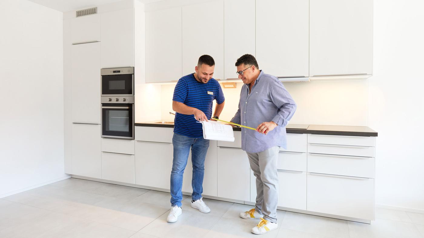 zwei Männer die in einen großen IKEA Küchenlösung stehen mit einem Maßband und einem Blatt Papier.