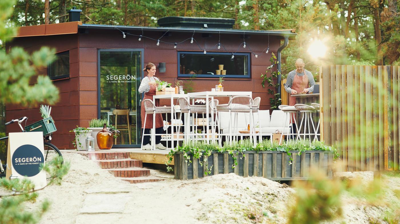 Zwei Personen richten ein Pop-up-Restaurant im Wald ein. Dazu stellen sie auf der Terrasse SEGERÖN Möbel für draussen auf.