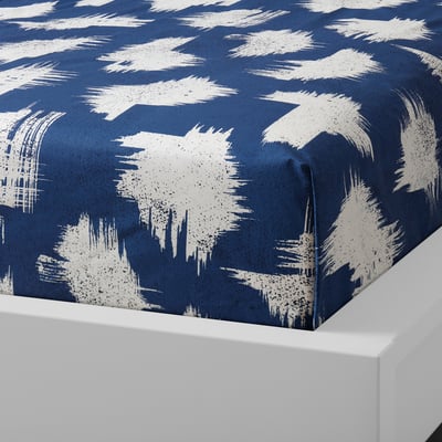 Blue bedspread with white brush strokes pattern, folded on white surface, showcasing soft cotton fabric.