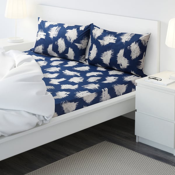 Bed with blue-white patterned sheets and a white pillow on a white bed frame.