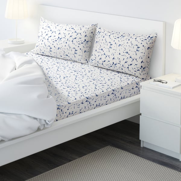Bed with patterned bed linens, two white lamps, and a white drawer set. The bed has blue and white patterned pillows and sheets.