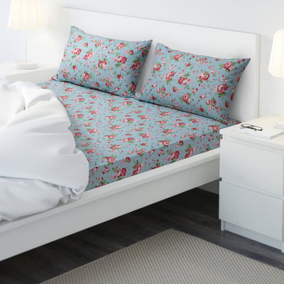 A bed with light blue floral sheet set. The bed is smaller than standard, with neatly arranged pillows, a white bed frame, and a bedside table.