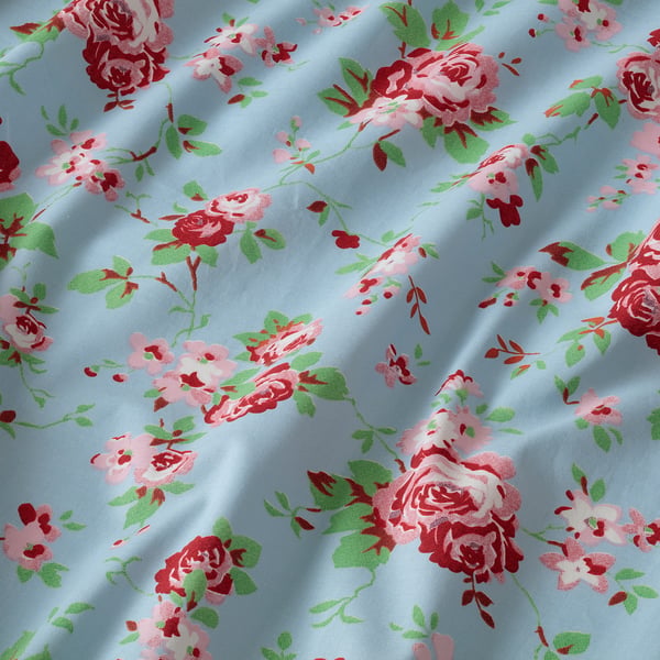 Floral fabric with light blue background, pink roses, green leaves, showcasing high-quality cotton texture.