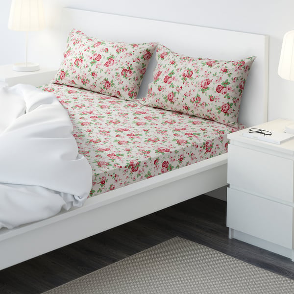 Made bed with floral sheet set, bedside table, lamp, book.