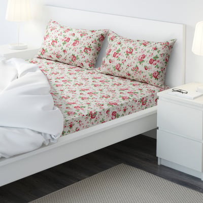 Made bed with floral sheet set, bedside table, lamp, book.