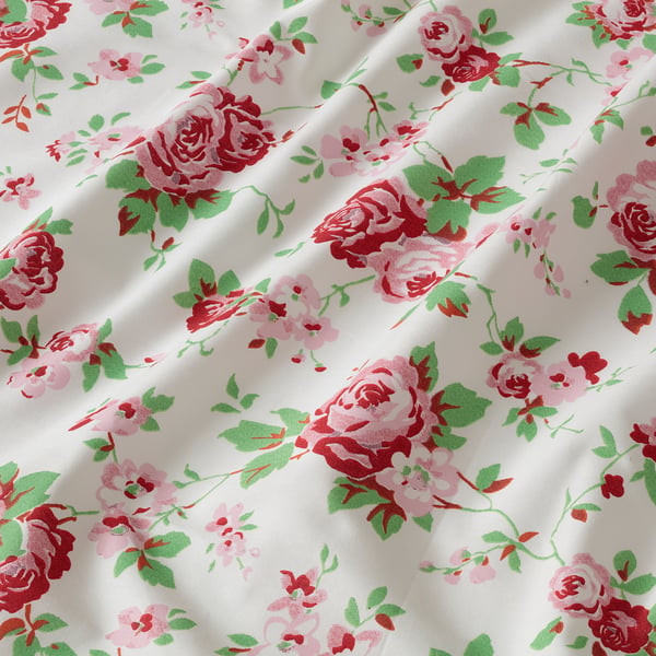 Floral fabric with red, pink roses and green leaves on white cotton, showcasing quality design and natural texture.