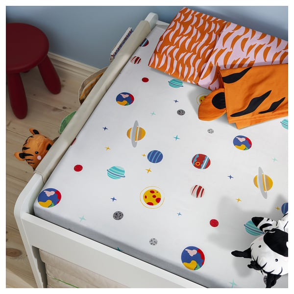 Baby bed with space-themed white sheets, colourful planets, and plush toys.