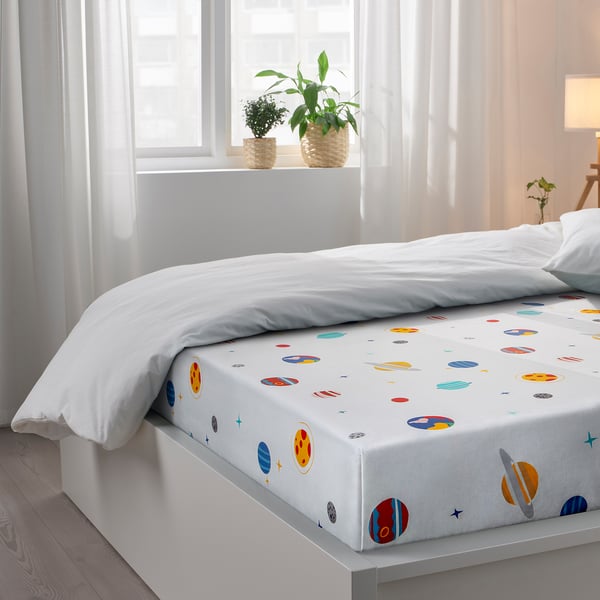 A decorative bed sheet with planets, stars, and moons print, enhancing a kid’s bedroom with a space theme.