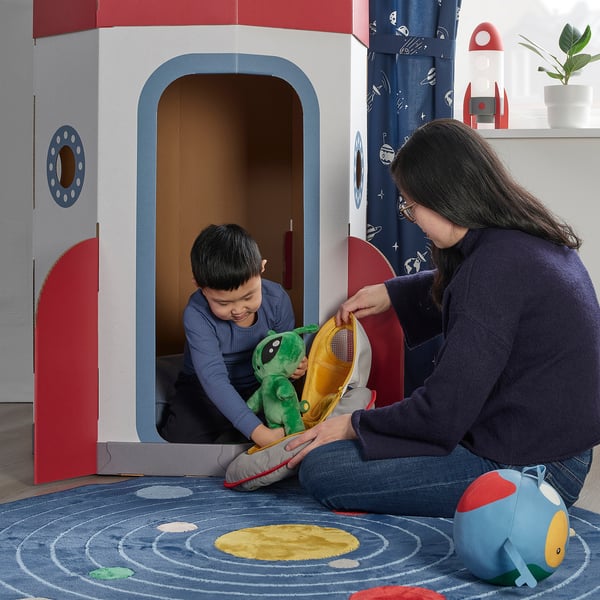 Person & child play with alien toy in cardboard spaceship.