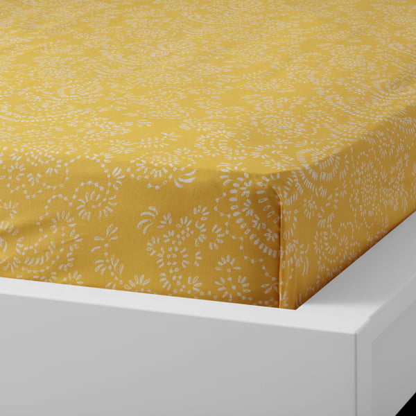 Bright yellow bed sheet with white floral pattern on white bed frame.