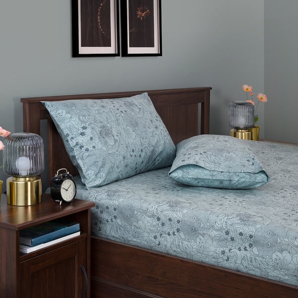 Cosy blue floral bedding set with wooden headboard, small bedside table with clock and lamp.