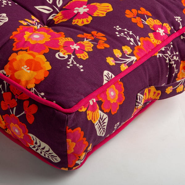 Floral floor cushion, vibrant colours on dark purple fabric, pink piping, soft and inviting texture.