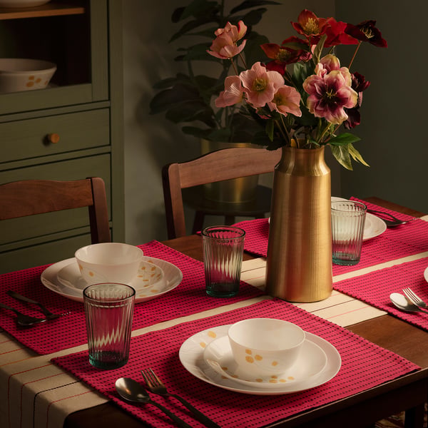 AROMATISK pink cotton placemat, 12x18, textured dobby weave, setting table with white dishes, pink glasses, gold vase, wooden chairs.
