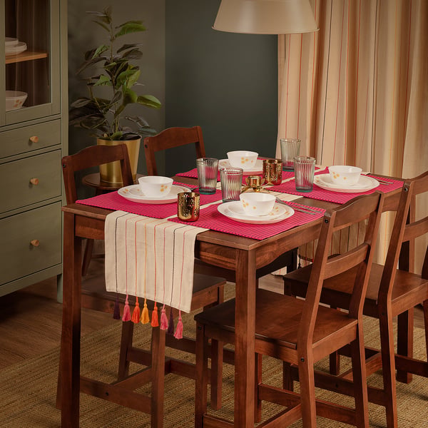 Brightly set table with AROMATISK runner, pink placemats, white cups, gold candlesticks.