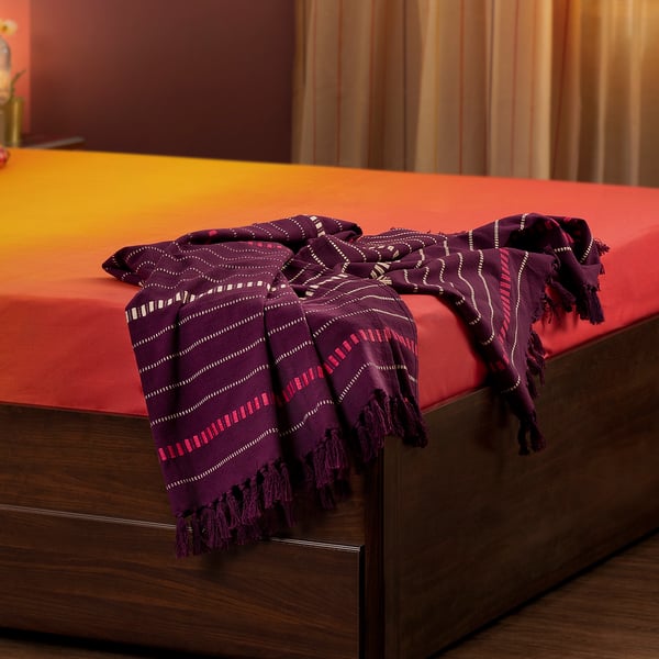 Purple cotton throw with stripes & fringes on a bed, contrasting orange & gold for warmth.
