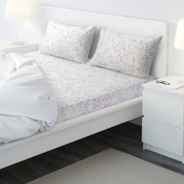 Minimalist bedroom with white bed, light purple floral ASKLÖNN sheet set, drawer unit, lamp, and rug.